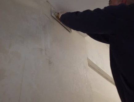 Un plâtrier travaille sur la finition des murs et des plafonds. En effet, il applique du plâtre pour obtenir des surfaces lisses