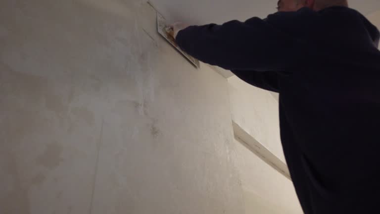 Un plâtrier travaille sur la finition des murs et des plafonds. En effet, il applique du plâtre pour obtenir des surfaces lisses